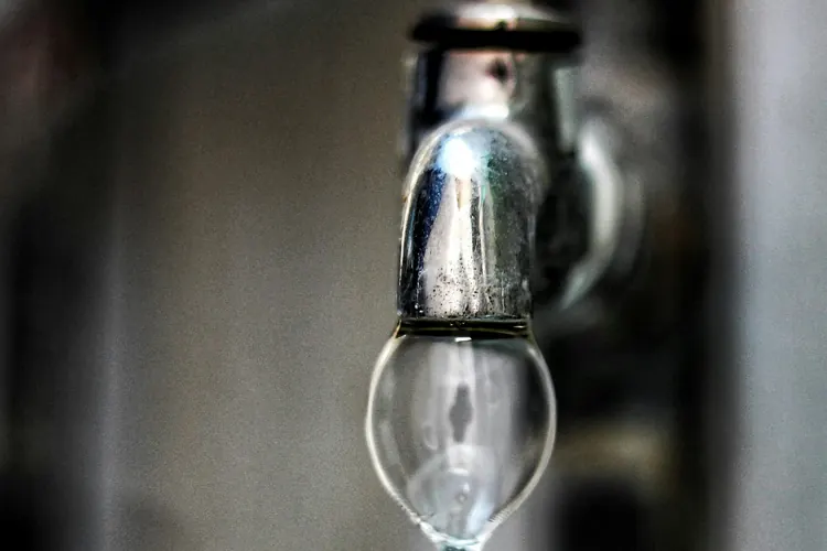Close-up of a faucet spout with water dripping and mineral spotting on the metal