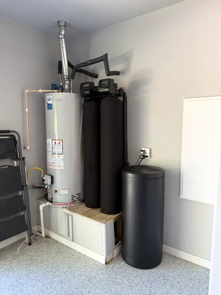 Garage water heater next to a whole-home water softener system with twin tanks and its brine tank
